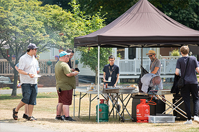 A group of learners standing around and serving food under a gazebo outside.