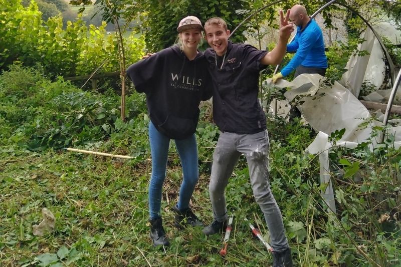 Students standing surrounded by trees and foliage, there is a large poly tunnel in the background