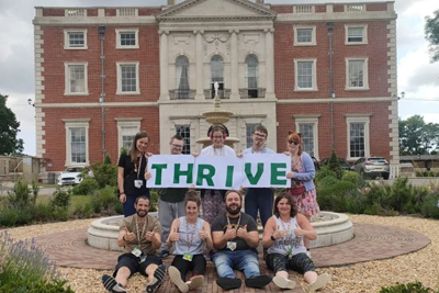Students and staff standing outside Merley House holding a banner reading THRIVE